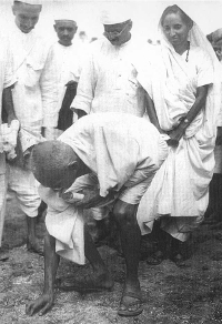 Gandhi a Dandi, al sud de Gujarat, recollint sal a la platja al final de la Marxa de la Sal, el 5 d'abril de 1930. Darrere d'ell es troba el seu segon fill Manilal Gandhi i Mithuben Petit. Autor desconegut - http://www.calpeacepower.org/0101/images/1930-pick-salt-GS_BG.jpg, Domini Públic, https://commons.wikimedia.org/w/index.php?curid=2082661